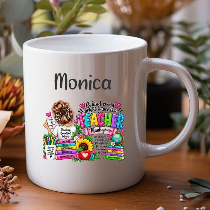 A white ceramic coffee mug with a colorful cartoon giraffe and the text 'Miss Periville I'M A TEACHER What's your SUPERPOWER?' printed on it, shown on a wooden surface with blurred plants in the background.
