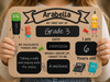 A child holds a personalized wooden sign with cartoon school-themed illustrations and handwritten-style text reading with personalised name, 'Grade 3', date, age, and favorite things. The child's hands and part of their clothing are visible.