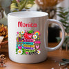 A white ceramic coffee mug with a colorful cartoon dog graphic and the text 'Mr Clarke TEACHERS MAKE THE WORLD A BRIGHTER PLACE', shown on a wooden surface with blurred plants in the background.