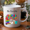 A white ceramic mug with a custom printed design featuring a cartoon kangaroo and the text 'Mr Jules TEACHERS MAKE THE WORLD A BRIGHTER PLACE', set on a wooden table with a blurred background of plants and decor.