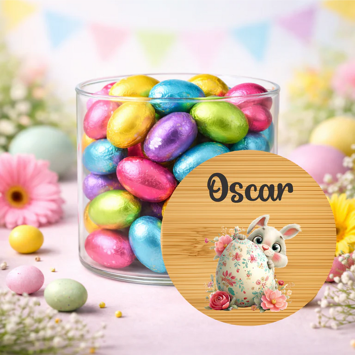 Jar of colorful Easter eggs with a personalized wooden plaque featuring a rabbit and floral design, on a pastel background.