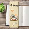 A personalized wooden bookmark featuring a cartoon dinosaur hatching from an egg, personalised at the top, and a bone illustration, displayed on a rustic wooden table next to an open notebook and a green succulent.