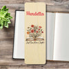 A personalized wooden bookmark personalised in red and an illustration of an open book with flowers, placed on top of an open book on a rustic wood surface with a small succulent.