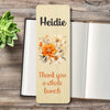 A personalized wooden bookmark  with floral illustration, placed on top of an open book on a rustic wood surface with a small succulent.