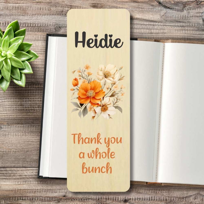 A personalized wooden bookmark  with floral illustration, placed on top of an open book on a rustic wood surface with a small succulent.