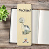 A personalized wooden bookmark featuring a cartoon long-neck dinosaur and the name printed on it, styled on top of an open notebook with a small succulent in the corner.