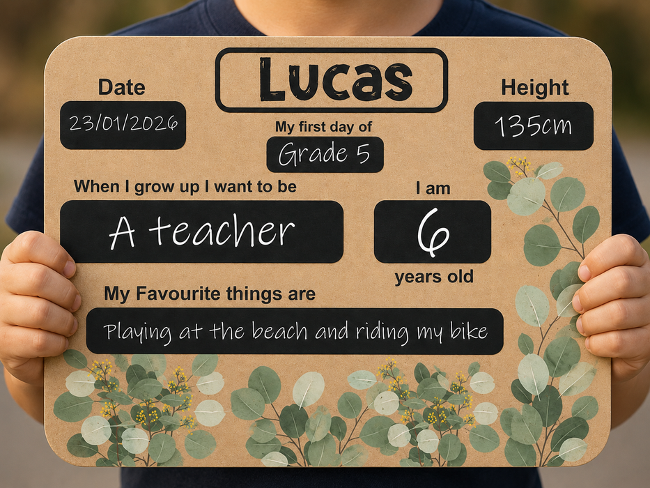 A child holds a personalized sign with rounded corners, featuring a tan background, black text boxes, and green eucalyptus illustrations. 