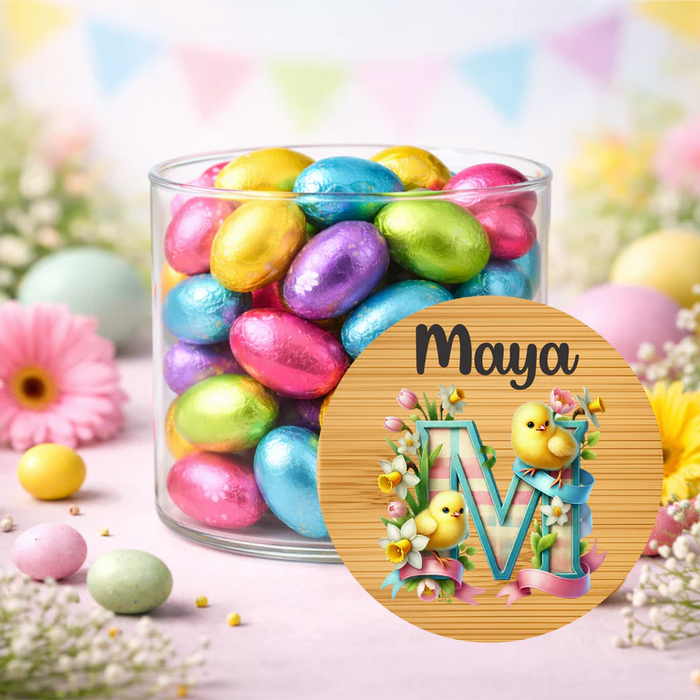 Jar of colorful Easter eggs with a decorative round sign featuring the name 'Maya' and a floral design.