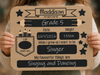 A child holds a personalized sign with school-themed graphics and text, including the name Grade 5, date, height, and aspirations. The sign has a kraft-paper background with black panels, stars, pencil illustrations, and white text.