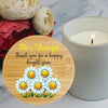 A round bamboo lid candle in a glass jar with a personalized message and smiling daisy illustration, styled next to a lit white candle and flowers on a marble surface.