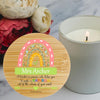 A round wooden bamboo candle keepsake with a colorful rainbow illustration and the personalised  text 'Mrs Archer A teacher is someone who helps you to make a RAINBOW out of the colours of your mind.' It is styled on a marble surface next to a lit candle and red flowers.