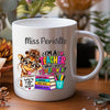 A white ceramic coffee mug with a colorful cartoon giraffe and the text 'Miss Periville I'M A TEACHER What's your SUPERPOWER?' printed on it, shown on a wooden surface with blurred plants in the background.