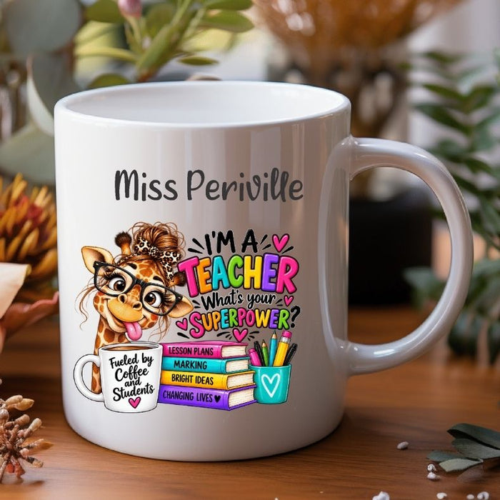 A white ceramic coffee mug with a colorful cartoon giraffe and the text 'Miss Periville I'M A TEACHER What's your SUPERPOWER?' printed on it, shown on a wooden surface with blurred plants in the background.